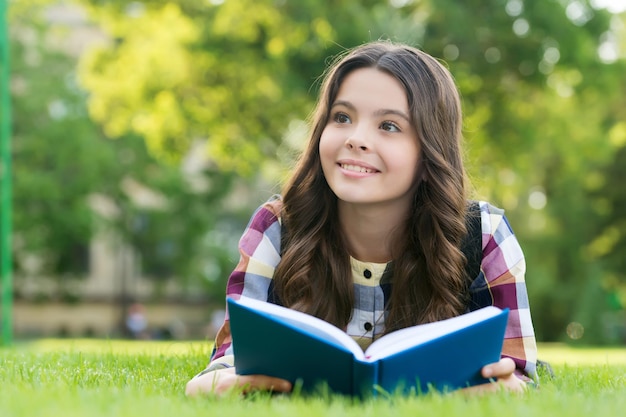 La lecture aide votre graine de connaissance à grandir. Un enfant heureux a lu un livre allongé sur l'herbe verte. Journée du savoir. 1er septembre. Retour à l'école. Enseignement primaire. Bibliothèque de l'école. Club périscolaire. Développez votre esprit.