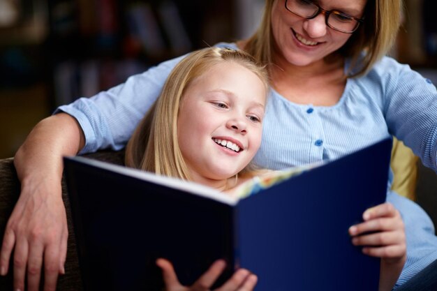 La lecture exerce le cerveau Une jolie jeune fille assise à côté de sa mère pendant qu'ils lisent un livre