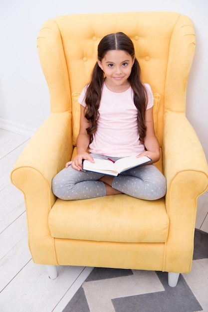 Lecture passe-temps utile Fille enfant s'asseoir fauteuil jaune lire livre Enfant rat de bibliothèque mignon Moment agréable dans une chambre confortable Fille enfant pyjama mignon se détendre lire un livre de conte de fées avant de dormir Encourager les habitudes utiles