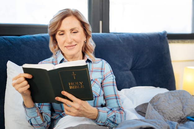 Lecture réfléchie. Femme mûre curieuse attentive lisant un livre sacré au cours de sa routine matinale quotidienne