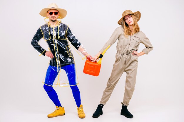 Élégant couple d'homme et femme en chapeaux de paille posant avec arrosoir sur mur blanc