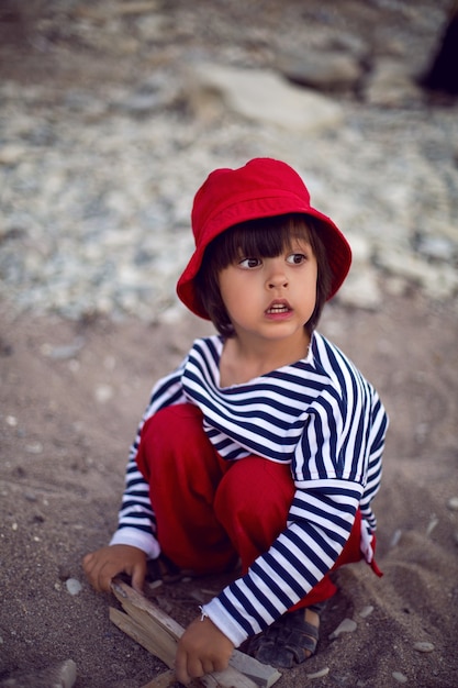 Élégant garçon enfant dans un gilet s'asseoir sur une plage de galets au bord de la mer en été