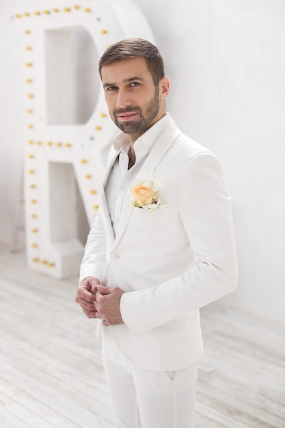 Élégant jeune bel homme avec une barbe dans un costume classique blanc