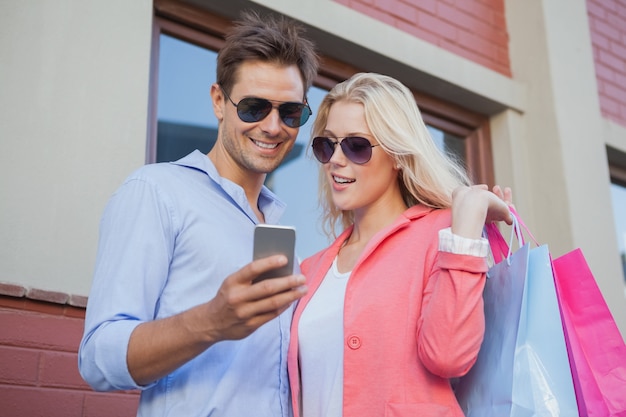 Élégant jeune couple regardant smartphone tenant des sacs à provisions