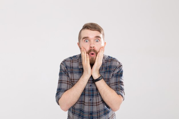 Élégant jeune homme hipster avec une moustache et une barbe ouvre joyeusement sa bouche sur un fond blanc