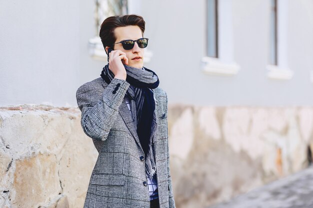 Élégant jeune homme à lunettes de soleil avec téléphone sur rue