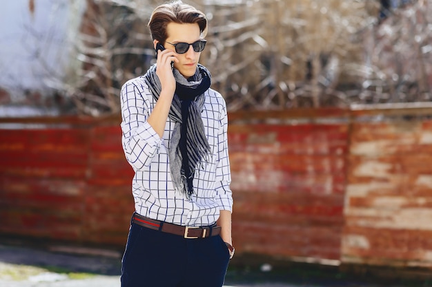 Élégant jeune homme à lunettes de soleil avec téléphone sur rue