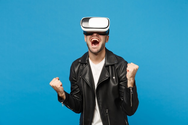 Élégant jeune homme mal rasé en t-shirt blanc veste noire regardant dans un casque, réalité virtuelle vr isolé sur fond de mur bleu portrait en studio. Concept de mode de vie des émotions des gens. Maquette de l'espace de copie.