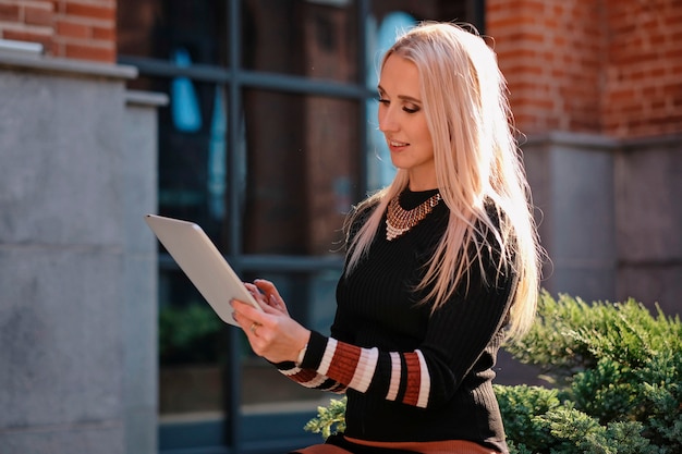 Élégante belle femme d'affaires aux cheveux blonds tenant un tablet pc, à l'extérieur