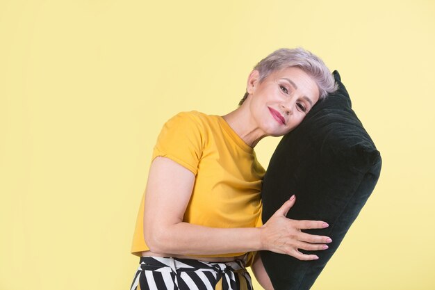 Élégante belle femme âgée avec un oreiller dans les mains sur un fond jaune