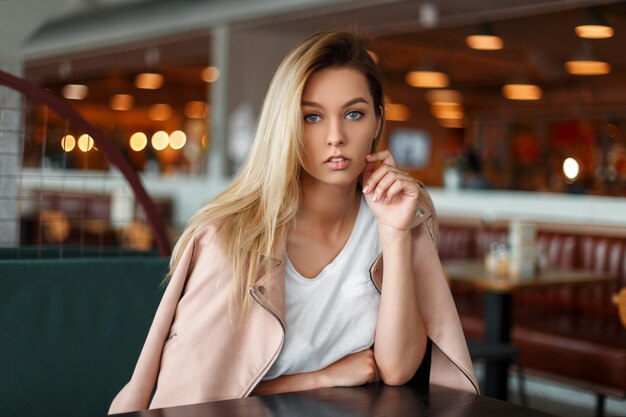 Élégante belle jeune femme dans une veste de mode rose assis à l'intérieur