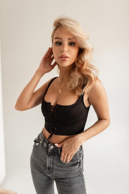 Élégante belle jeune femme sexy aux cheveux blonds dans un t-shirt noir fashion et un jean vintage sur fond blanc en studio