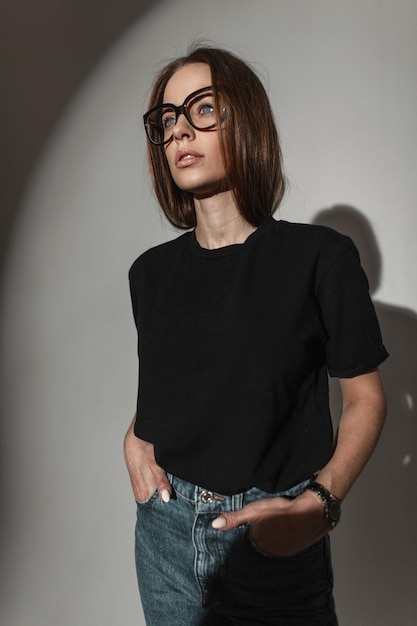 Élégante belle jeune fille glamour avec des lunettes à la mode dans un t-shirt noir maquette pour la conception en studio