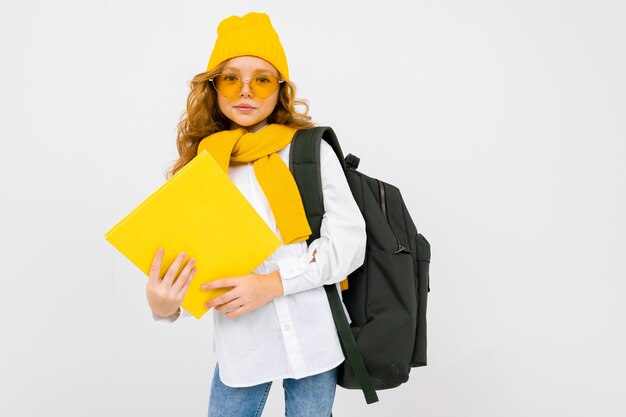 Élégante écolière de charme caucasien dans une chemise blanche, avec un chapeau et un sac à dos avec un cahier dans ses mains sur blanc