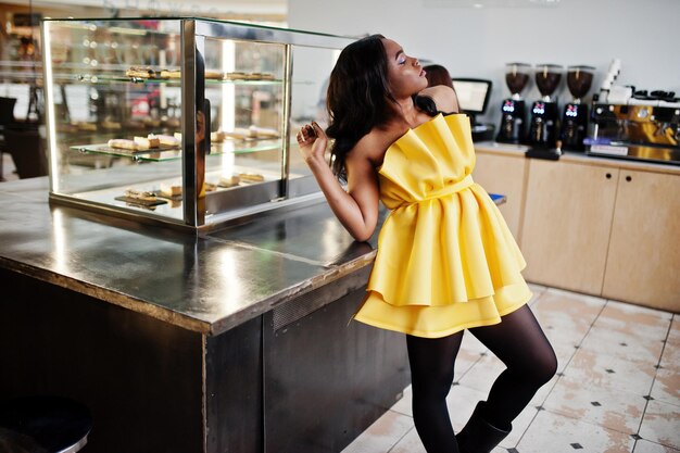 Élégante femme afro-américaine à la robe jaune posée au café