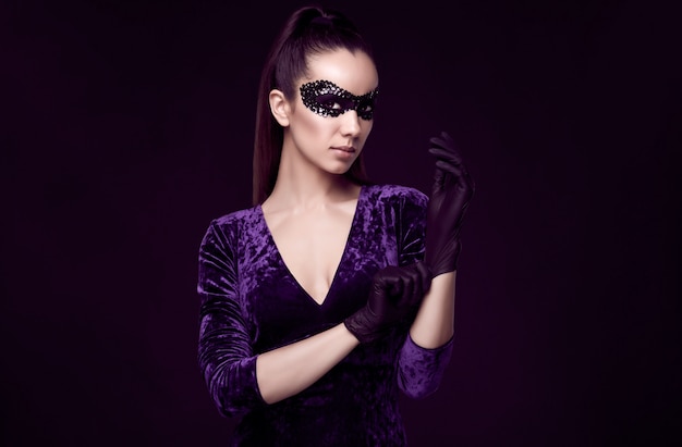Élégante femme brune en belle robe violette et masque de paillettes gant