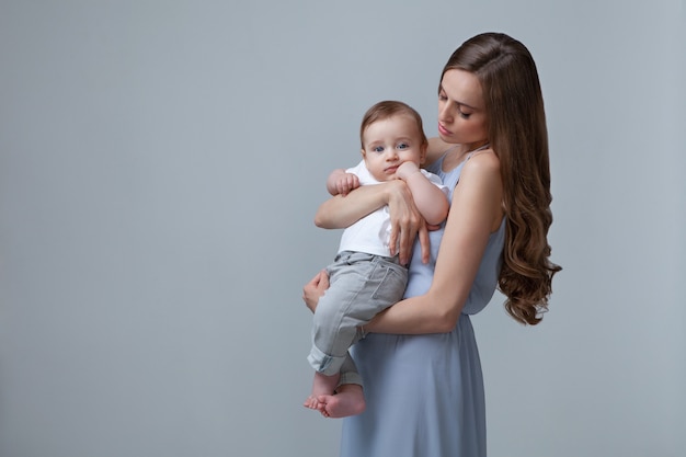 Élégante femme tenant un petit bébé isolé sur fond bleu Belle mère et fils modèle caucasien