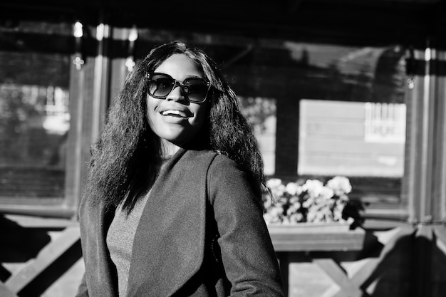 Élégante fille afro-américaine en manteau bleu et lunettes de soleil posées à la journée d'automne ensoleillée Afrique modèle femme