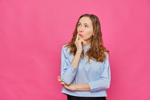 Élégante fille caucasienne dans un t-shirt bleu pâle rêver regarde ailleurs un objet abstrait sur rose