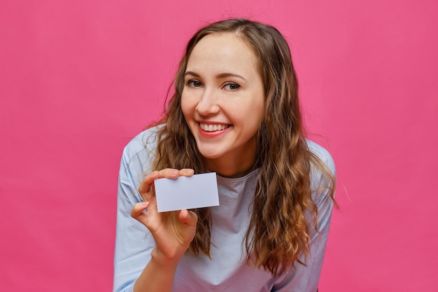 Élégante fille caucasienne tenant une carte blanche dans ses mains sur un fond rose