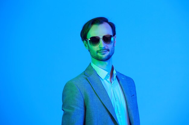 Élégante jeune bel homme à lunettes de soleil et en veste grise élégante Portrait de mode Studio