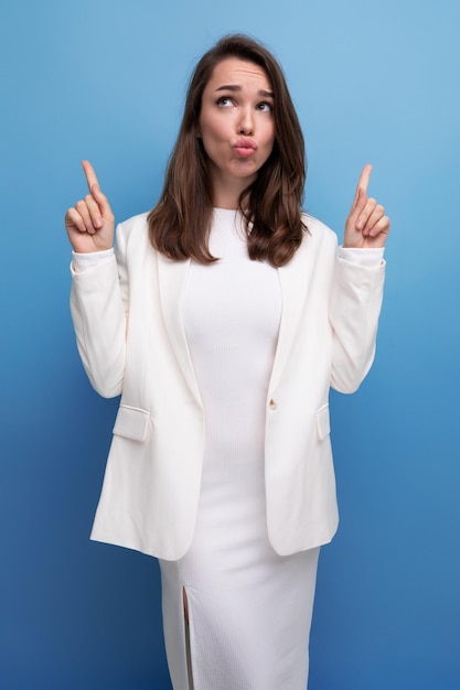 Élégante jeune brune aux cheveux longs femme en robe blanche pointe son doigt sur le côté