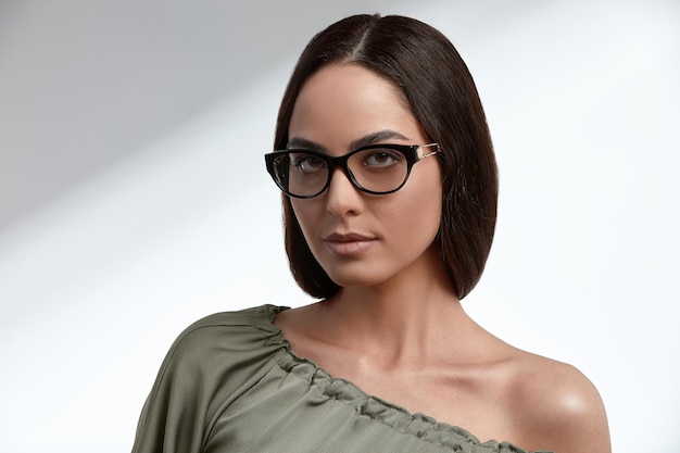 Élégante jeune brune vêtue d'une robe verte et de lunettes, couverture de magazine, industrie de la mode, femme d'affaires prospère.