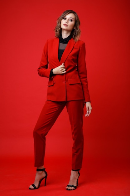 Élégante jeune femme en costume rouge veste pantalon pantalon chemisier noir sur fond Monochrome