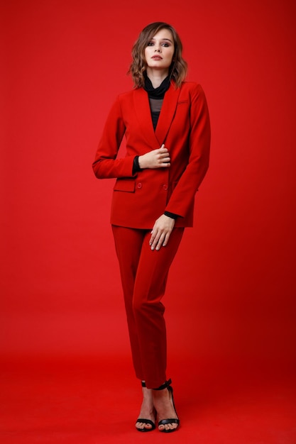 Élégante jeune femme en costume rouge veste pantalon pantalon chemisier noir sur fond Monochrome