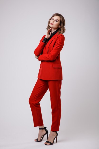 Élégante jeune femme dans un joli costume rouge veste pantalon pantalon chemisier noir sur fond blanc