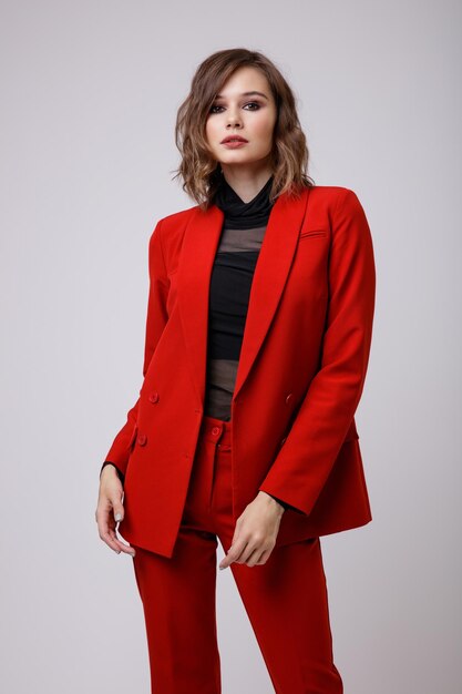 Élégante jeune femme dans un joli costume rouge veste pantalon pantalon chemisier noir sur fond blanc