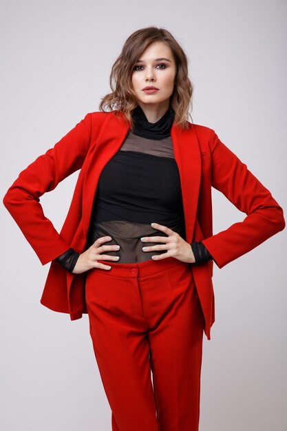 Élégante jeune femme dans un joli costume rouge veste pantalon pantalon chemisier noir sur fond blanc