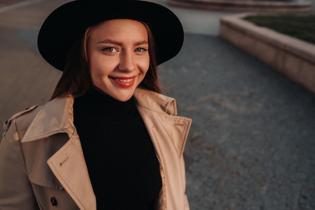 Élégante jeune femme dans un manteau beige dans un chapeau noir dans une rue de la ville. Mode de rue pour femmes. Vêtements d'automne Style urbain.