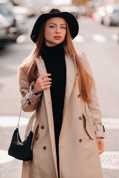 Élégante jeune femme dans un manteau beige dans un chapeau noir dans une rue de la ville. Mode de rue pour femmes. Vêtements d'automne Style urbain.