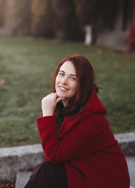 Élégante jeune femme dans un manteau décontracté bordeaux en automne Joli modèle se promène dans le parc en automne doré à travers des arbres colorés et des feuilles mortes Automne promenade nature colorée