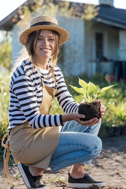 Élégante jeune femme jardinier tenant une plante avant de planter dans le jardin