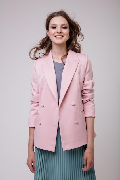 Élégante jeune femme en joli costume, blazer veste rose pâle, jupe verte posant sur fond blanc