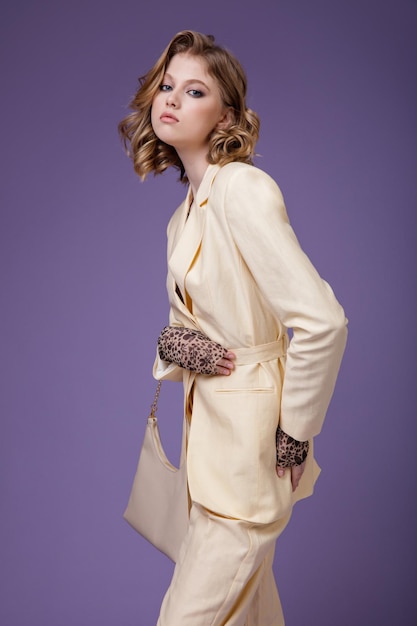 Élégante jeune femme en lin crème beige veste pantalon blazer handbad sur fond violet