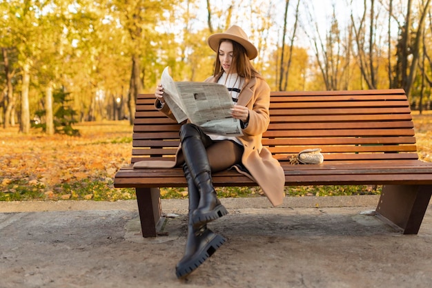 Élégante jeune femme lisant le journal dans le parc d'automne