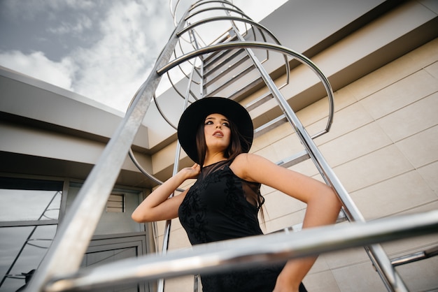 Élégante jeune femme posant dans un chapeau sur l'escalier de secours du centre d'affaires. Mode
