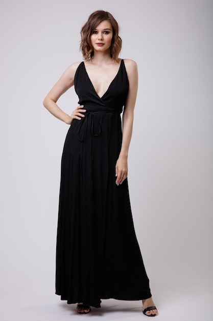 Élégante jeune femme en robe de soirée noire avec un décolleté profond sur fond blanc