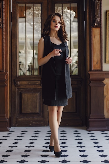 Élégante jeune femme en robe de soirée noire posant dans un intérieur vintage. Tir de mode.