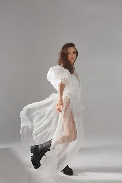 Élégante jeune femme vêtue d'une robe blanche flottante et de chaussures hautes fille modèle haute couture en tr...