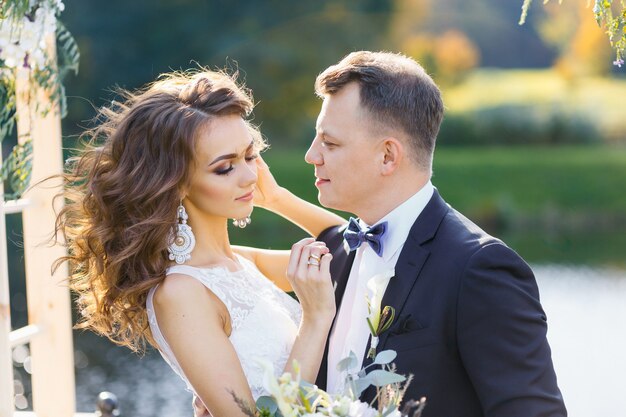 Élégante mariée bouclée et heureux marié à l'extérieur sur le fond du lac. Cérémonie de mariage élégante et créative