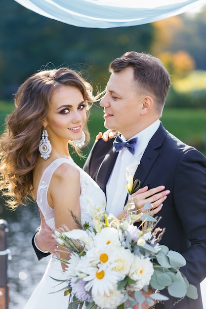 Élégante mariée bouclée et heureux marié à l'extérieur sur le fond du lac. Cérémonie de mariage élégante et créative