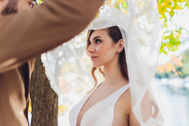 Élégante mariée et le marié heureux posant au grand mot d'amour dans la lumière du soir à la réception de mariage en plein air. Magnifique couple de mariage de jeunes mariés s'amusant dans le parc du soir.