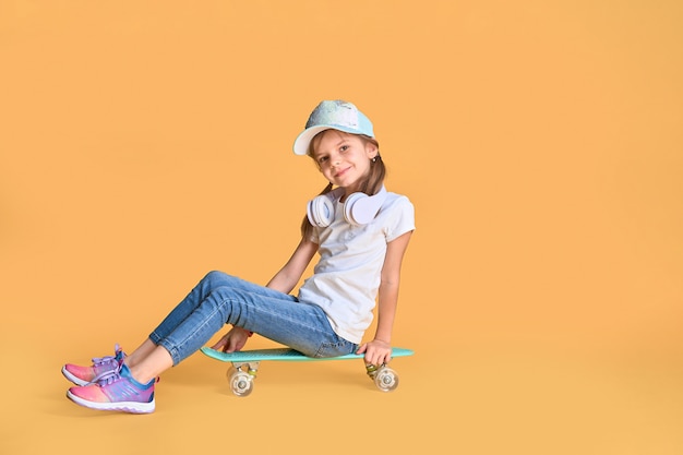 Élégante petite fille enfant fille décontractée avec skateboard sur mur jaune