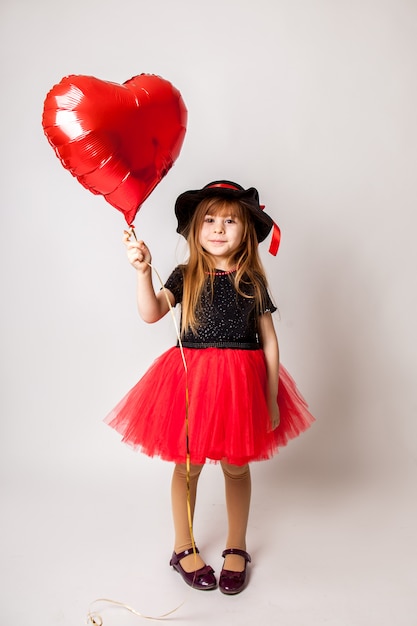 Élégante petite fille sur une robe rouge tenant une boule rouge en forme de coeur.