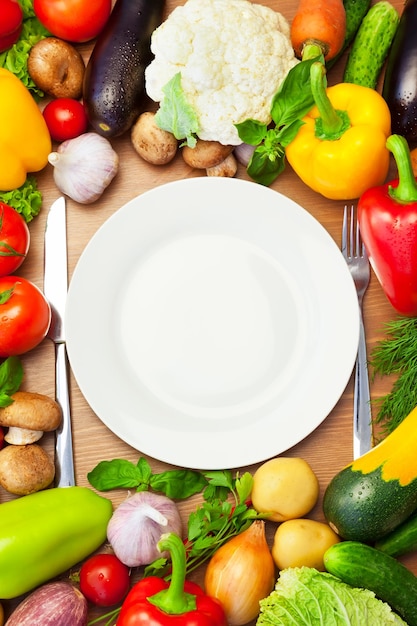 Légumes biologiques autour d'une assiette blanche avec couteau et fourchette