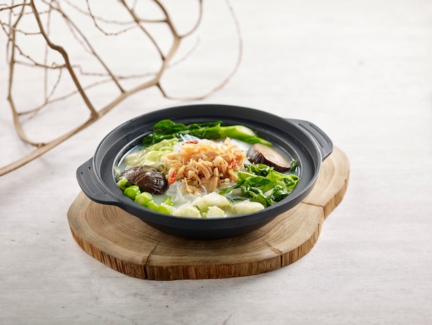 Légumes braisés et conpoy avec vermicelles dans une soupe de poisson servis dans une cocotte servis dans un plat isolé sur une planche de bois vue latérale sur fond gris